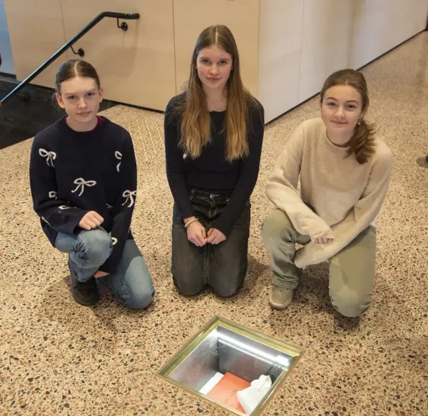 Tre jenter sitter på kne ved grunnsteinen som er nedfelt i golvet på Anno Domkirkeodden historiesenter. Fra venstre: Anbjørg Westad Skjelseth, Ringsaker, Signe-Jarlene Larsen, Løten, og Vilde Svartnes Andersen, Stange.