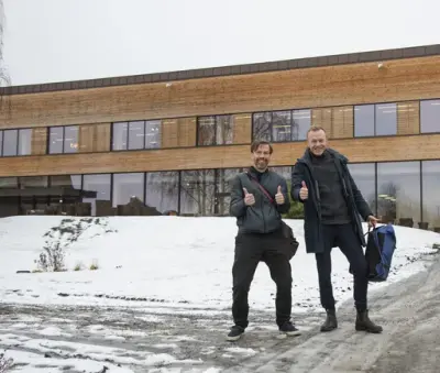 Arkitektene Kristian Langkilde og Kasper Lorentzen viser tomler opp foran hovedinngangen til sitt bygg "Shelter".