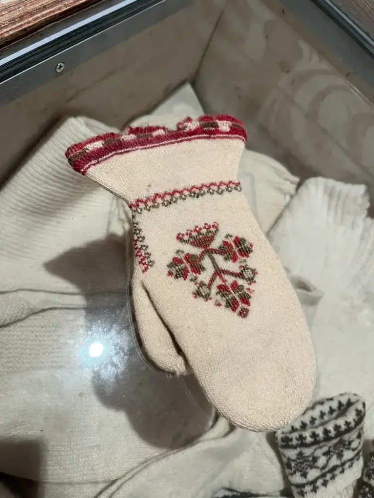 En hvit strikket vott med symetrisk mønster brodert inn.