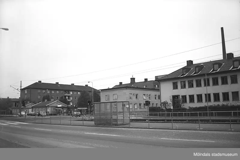 Fotografiet är taget någon gång under 1970-talet och vi ser i bakgrunden till vänster Mölndals lasarett/ Mölndals sjukhus bägge låga flygelbyggnader som invigdes med sjukhusbyggnaden 1924. Dessutom skymtar även den tillbyggnad som sjukhuset lät göra senare och som är invigd år 1954 (till vänster i bakgrunden). 

Lägg märke till kiosken som ligger till höger om kortändan till den flygelbyggnad som befinner sig närmast i bild.

Vi ser biltreafik som går in mot Mölndalsbro.

Spårvagnshållplatsen är Mölndals lasarett.