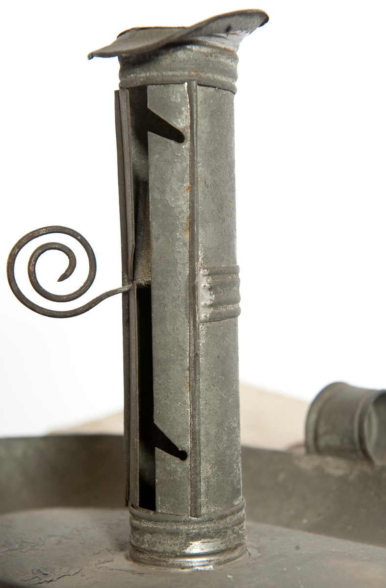 Modellexemplar av ljusstake, av bleckplåt med fat och hållare för vaxljus, 3 lägen, samt handtag. Vidhäftad etikett med sigill med texten "Kong. Förwaltningens af Sjö-Ärenderne faststälde modell på ljusplåtar enkel af bleck. För Kongl. Flottans behof. Stockholm d. 19 oct. 1828. På befallning Carl Servais"