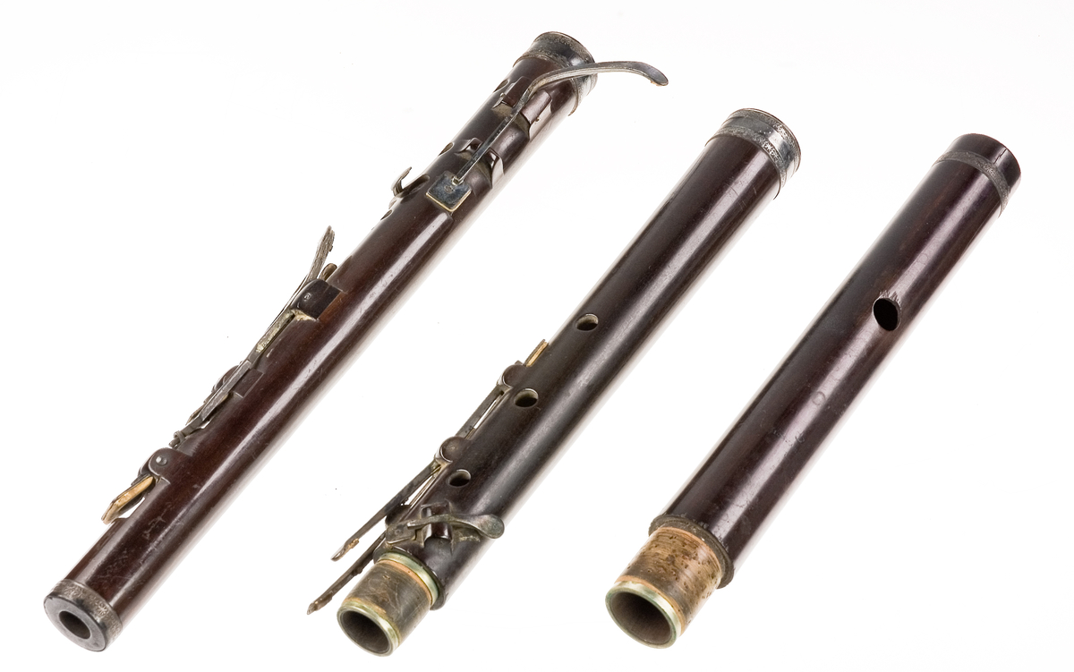 Tvärflöjt i ebenholts med ringar av silver och mörkt horn, med blommönster. 3 delar. C-fot. 8 klaffar med bocklagring och kvadratiska plattor, varav 2 reglerar samma ton: B.