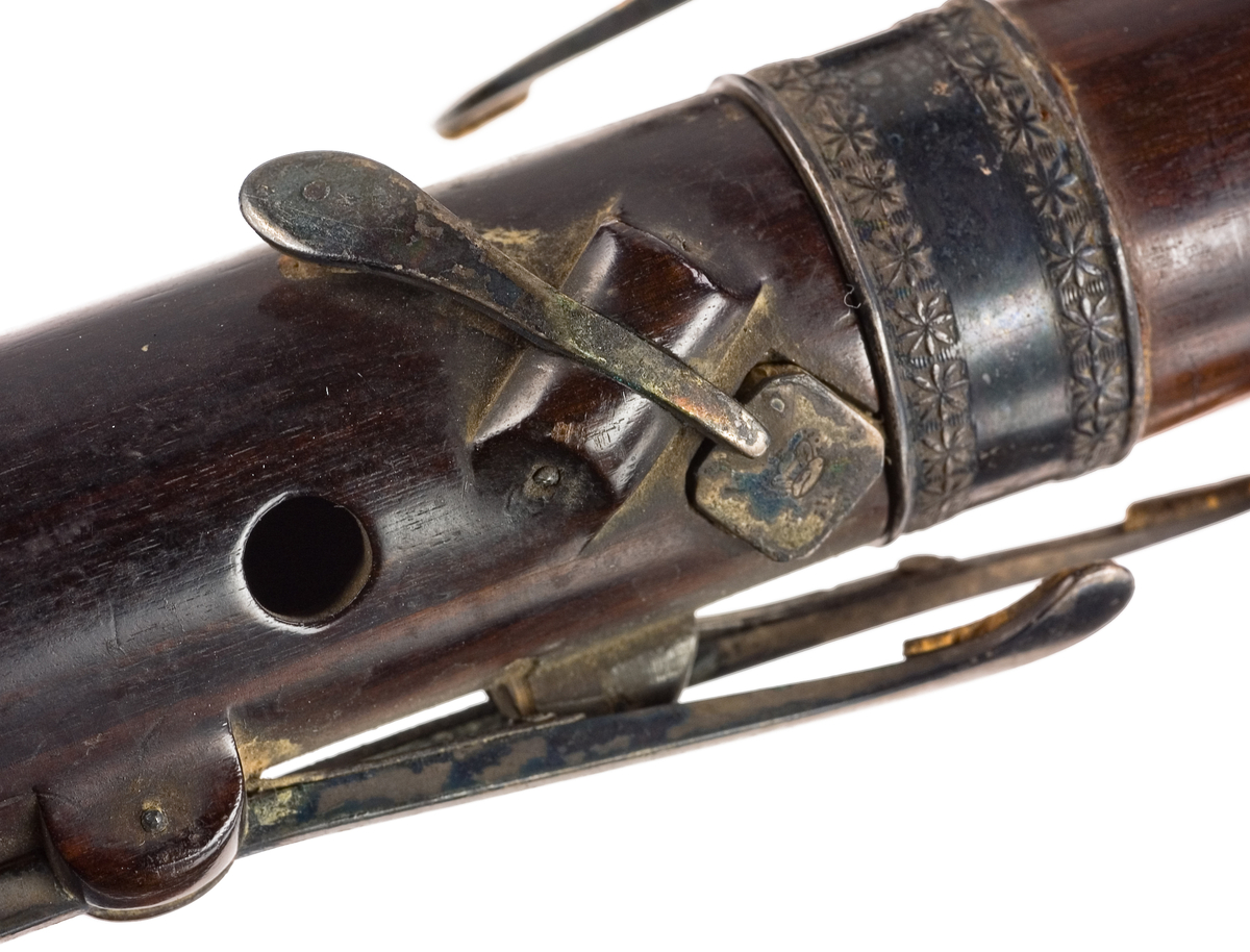 Tvärflöjt i ebenholts med ringar av silver och mörkt horn, med blommönster. 3 delar. C-fot. 8 klaffar med bocklagring och kvadratiska plattor, varav 2 reglerar samma ton: B.