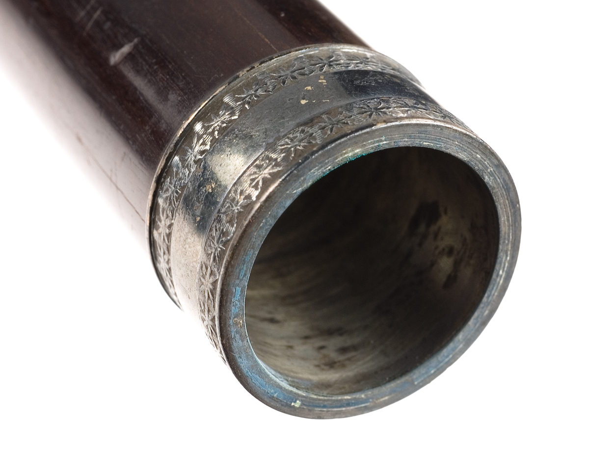 Tvärflöjt i ebenholts med ringar av silver och mörkt horn, med blommönster. 3 delar. C-fot. 8 klaffar med bocklagring och kvadratiska plattor, varav 2 reglerar samma ton: B.