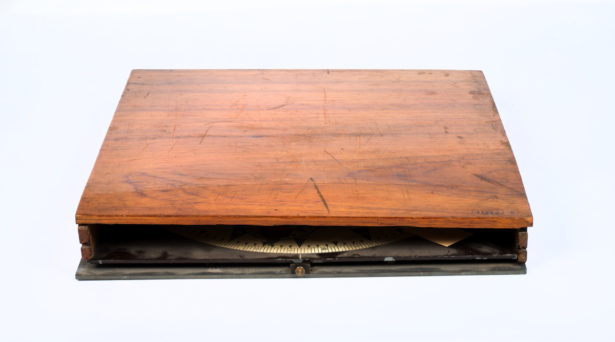 Kollisions-tavla, Ekelöfs patent, bestående av vit kompasssros med två rörliga farygsmodeller jämte visare, fästade till en rund bottenplatta, alltsammans monterat till en brunmålad, fyrkantig bottenplatta med lock av mahogny. Tillhörande tryckt beskrivning. Stockholm, 1892.