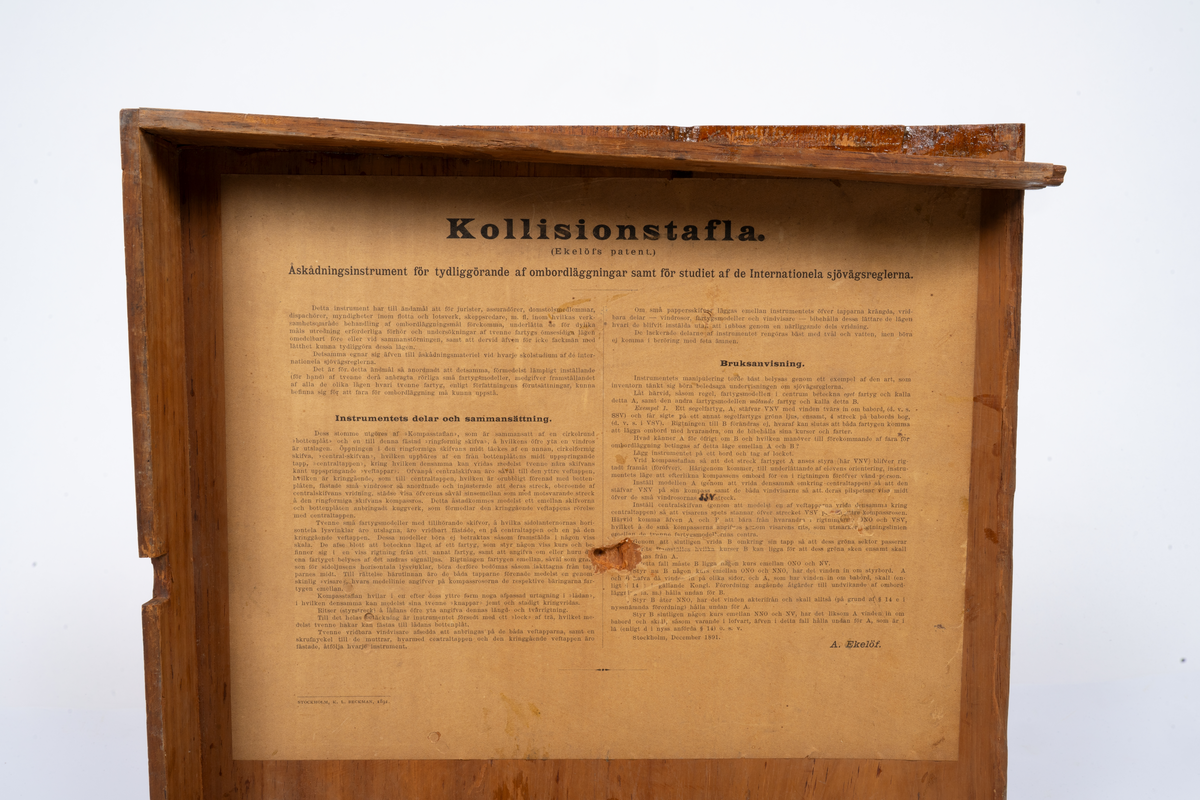 Kollisions-tavla, Ekelöfs patent, bestående av vit kompasssros med två rörliga farygsmodeller jämte visare, fästade till en rund bottenplatta, alltsammans monterat till en brunmålad, fyrkantig bottenplatta med lock av mahogny. Tillhörande tryckt beskrivning. Stockholm, 1892.