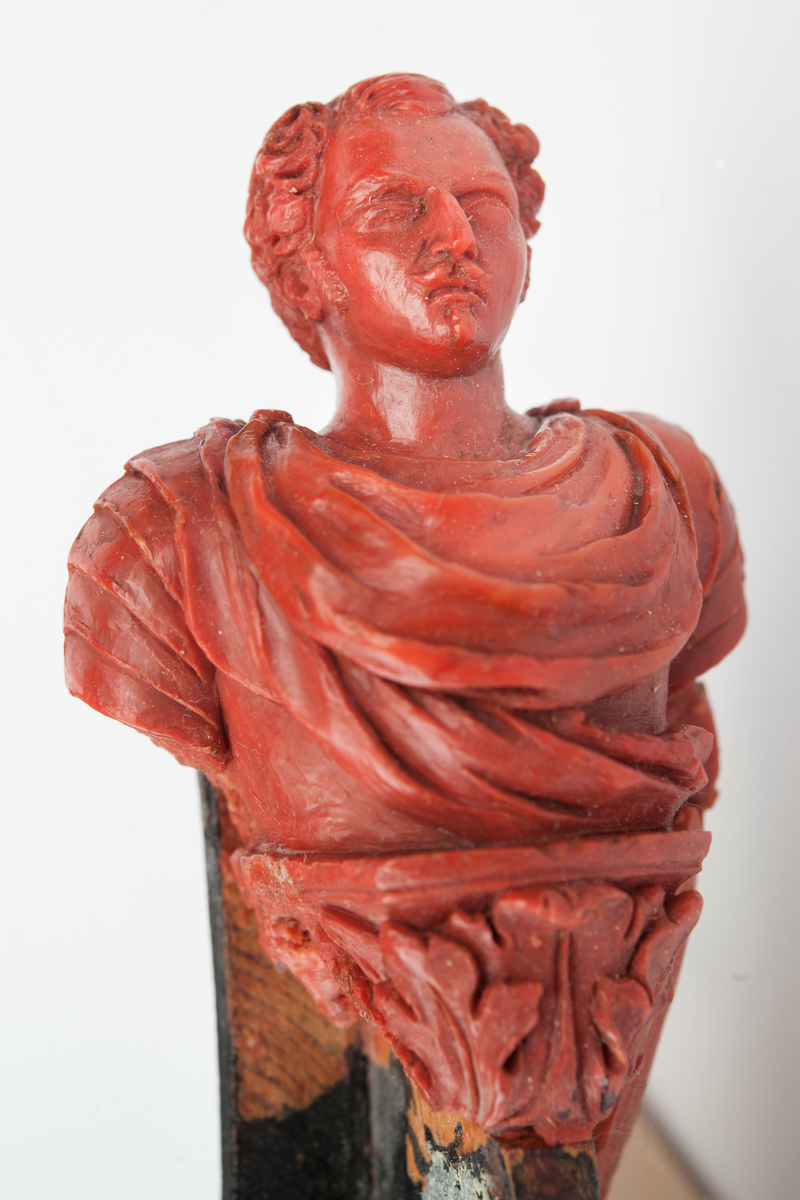 Förslag till galjon till PRINS OSCAR.
Bröstbild av Prins Oscar på sockel prydd med akantusblad och flankerad om babord med krönt sköld, skisserad. Monterad till stävkonstruktion av svartmålat trä. Röd vax, förslag