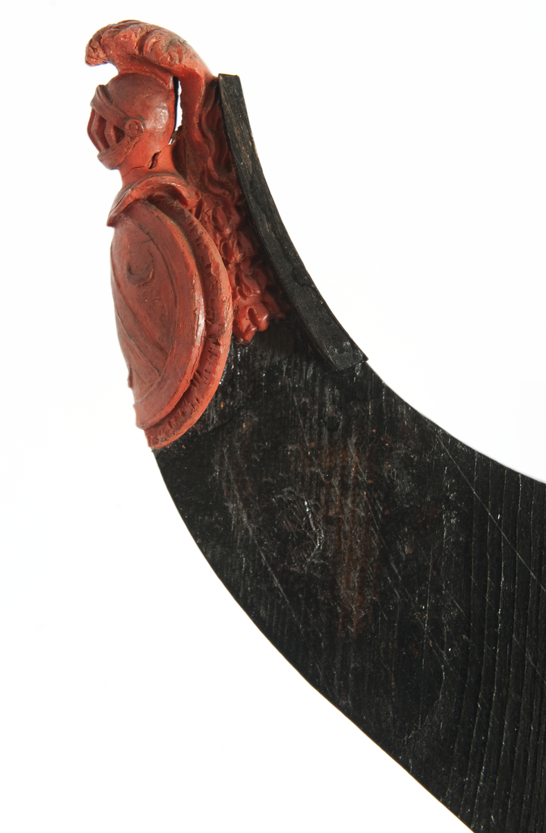 Föreställande fregatten AF CHAPMANs galjon. Vapensköld, oval med vinkel och tre halvmånar. Krönt av hjälm med fjäderbuske. På sidorna bladslinga samt om styrbord ett delfinhuvud. Monterat till stävkonstruktion av svartmålad träplatta, märkt ”Chapman”. 
Plattan: 155 x 85 mm röd vax