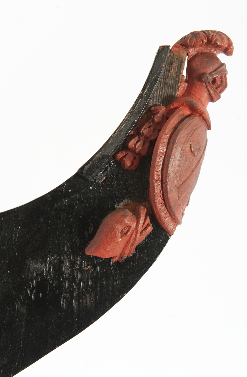 Föreställande fregatten AF CHAPMANs galjon. Vapensköld, oval med vinkel och tre halvmånar. Krönt av hjälm med fjäderbuske. På sidorna bladslinga samt om styrbord ett delfinhuvud. Monterat till stävkonstruktion av svartmålad träplatta, märkt ”Chapman”. 
Plattan: 155 x 85 mm röd vax