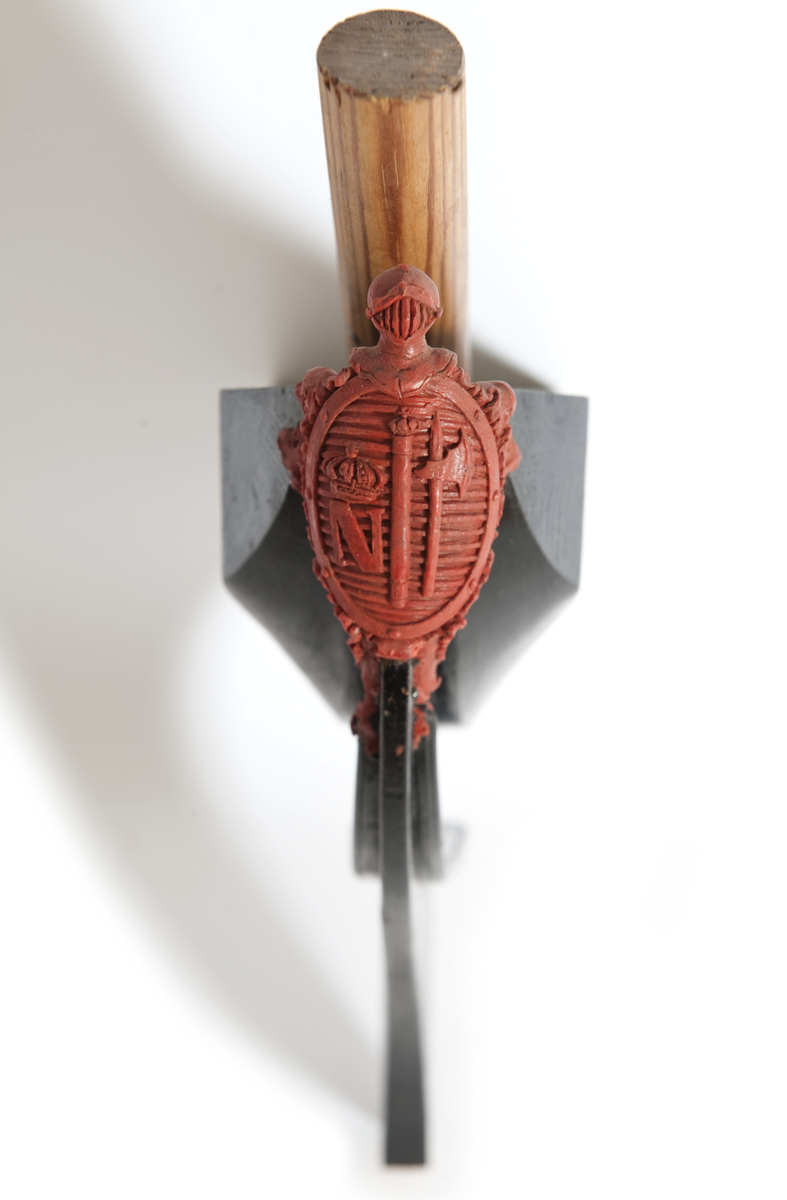 NORRKÖPINGs galjon. Vapensköld krönt av hjälm. På sköldens refflade botten krönt” N” kommandostäv och bila . På sidorna stiliserat bladverk. Monterad på stävkonstruktion av svartmålat trä, bogspröt. Omålat. röd vax