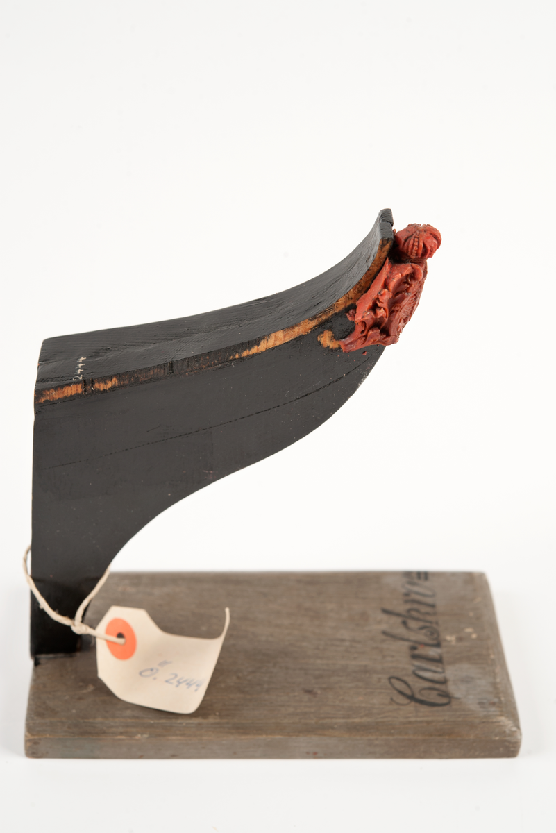 Föreställande korvetten KARLSKRONAs galjon. Stadsvapnet med kunglig krona över och bladverk på sidorna. Monterad till stävkonstruktion av svartmålat trä , fästad till gråmålad träplatta. Plattan: 170 x 85mm Korett. Röd vax.