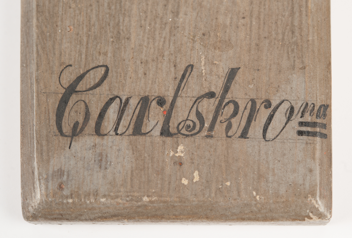 Föreställande korvetten KARLSKRONAs galjon. Stadsvapnet med kunglig krona över och bladverk på sidorna. Monterad till stävkonstruktion av svartmålat trä , fästad till gråmålad träplatta. Plattan: 170 x 85mm Korett. Röd vax.