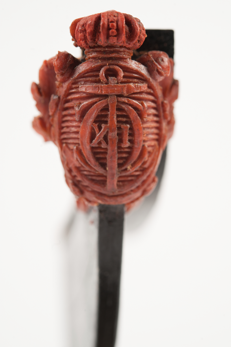 Föreställande korvetten KARLSKRONAs galjon. Stadsvapnet med kunglig krona över och bladverk på sidorna. Monterad till stävkonstruktion av svartmålat trä , fästad till gråmålad träplatta. Plattan: 170 x 85mm Korett. Röd vax.