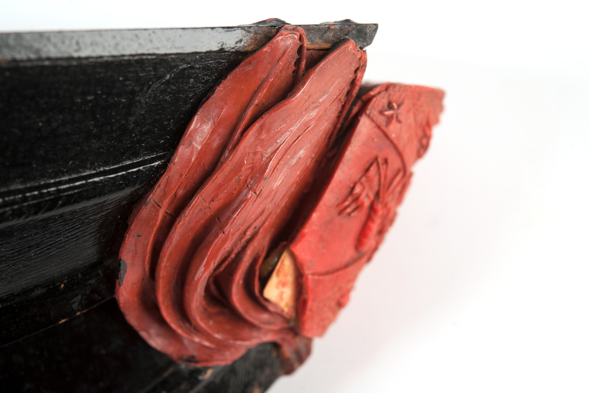 Föreställande korvetten LAGERBJELKEs vapensköld, omgiven av 2 flaggor på var sida. Monterad till stävkonstruktion av svartmålat trä med del av gråmålad bogspröt.
Röd vax.