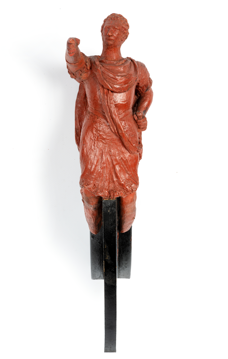 Förestäler Linjeskeppet Carl XIV Johans galjon. Mansfigur, Carl XIV Johan i  romersk dräkt. Höger arm avslagen. Monterad till
stävkonstruktion av svartmålat trä. Röd vax.