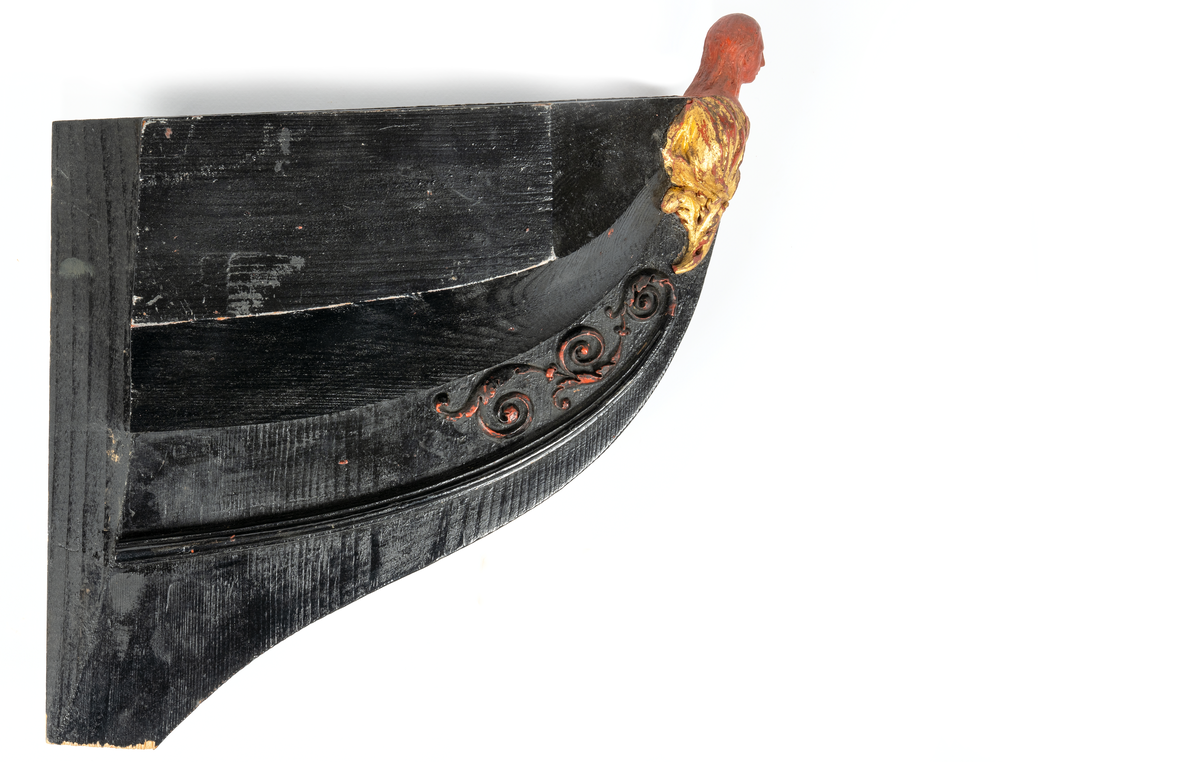 Korvetten EUGENIEs galjon. Kvinnobyst vilande på akantusblad. Nedtill om styrbord bladslinga. Huvudet skadat. Dräkt och blad förgyllda men röda vaxet synas. Monterad till stävkonstruktion av svartmålat trä. Röd vax.