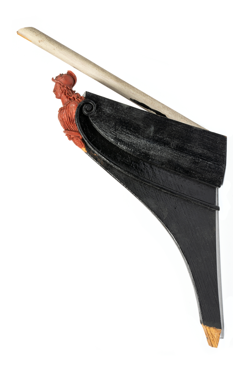 Chefsfartyget VALKYRIANs galjon. Kvinnobyst i grekisk  dräkt med hjälm, sockel med vapenplåt. Monterad  på stävkonstruktion av svartmålat trä, med del av gråvitmålat bogspröt. Allt på mörkgråmålad platta. 160X85 mm. Röd vax.