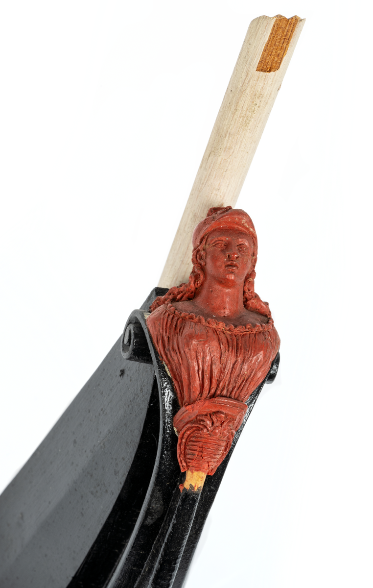 Chefsfartyget VALKYRIANs galjon. Kvinnobyst i grekisk  dräkt med hjälm, sockel med vapenplåt. Monterad  på stävkonstruktion av svartmålat trä, med del av gråvitmålat bogspröt. Allt på mörkgråmålad platta. 160X85 mm. Röd vax.