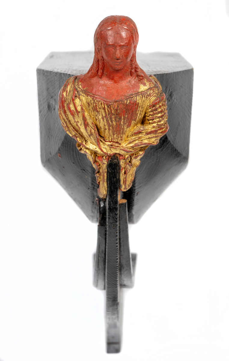 Korvetten EUGENIEs galjon. Kvinnobyst vilande på akantusblad. Nedtill om styrbord bladslinga. Huvudet skadat. Dräkt och blad förgyllda men röda vaxet synas. Monterad till stävkonstruktion av svartmålat trä. Röd vax.