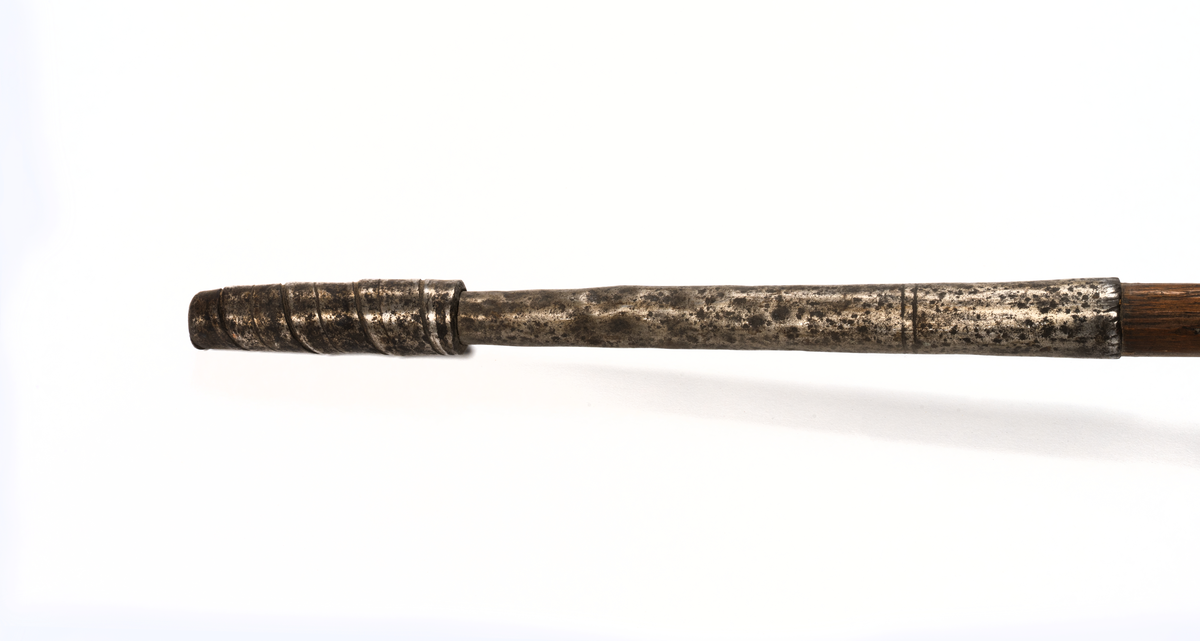 Hordapik, Afrika. Spets av smitt järn, bredbladig, tvåeggad med långt hylsfäste skaft av hårt träslag med lång doppsko av järnplåt nedtill virad till en klump.
Från fregatten VANADIS världsomsegling 1883-1885.
Gåva: Amiral Lindmans sterbhus 1937.