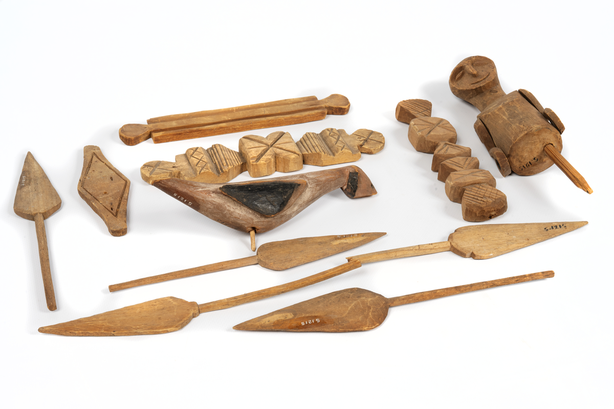 Modell av kanot från Samoa, skuren ur en stam av balsaliknande trä med relingen urhakad för tio tvärsgående balkar. Till modellen hör 5 snidade mansfigurer, fem paddlar, en fågel och fyra olika snidade tofter eller dylikt. Flera smärre skador. Större skada i aktern.