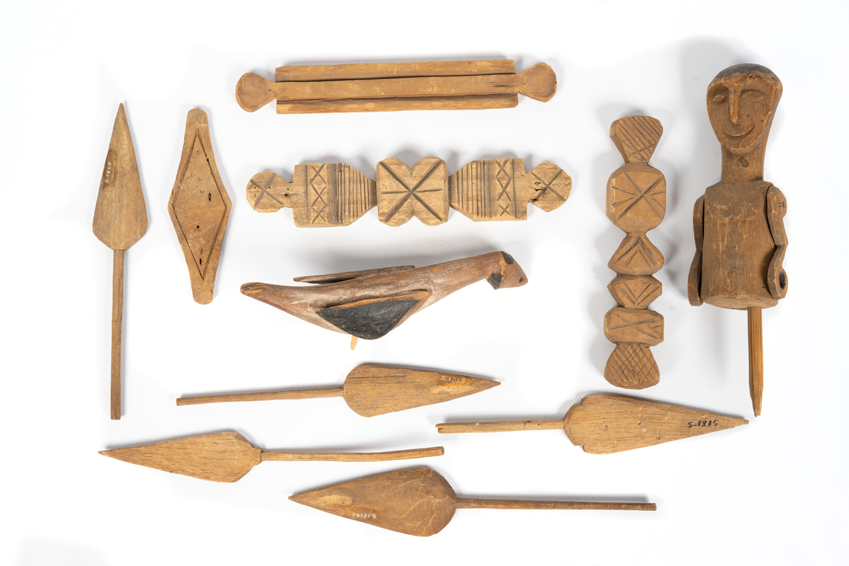 Modell av kanot från Samoa, skuren ur en stam av balsaliknande trä med relingen urhakad för tio tvärsgående balkar. Till modellen hör 5 snidade mansfigurer, fem paddlar, en fågel och fyra olika snidade tofter eller dylikt. Flera smärre skador. Större skada i aktern.