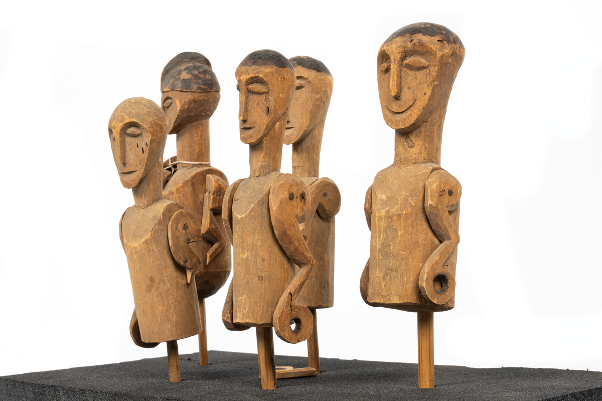 Modell av kanot från Samoa, skuren ur en stam av balsaliknande trä med relingen urhakad för tio tvärsgående balkar. Till modellen hör 5 snidade mansfigurer, fem paddlar, en fågel och fyra olika snidade tofter eller dylikt. Flera smärre skador. Större skada i aktern.