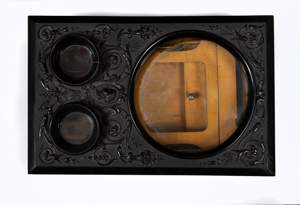 Svarlackad stereoskop med dekorerad ovansida och tre linser. Tillbehör finns.