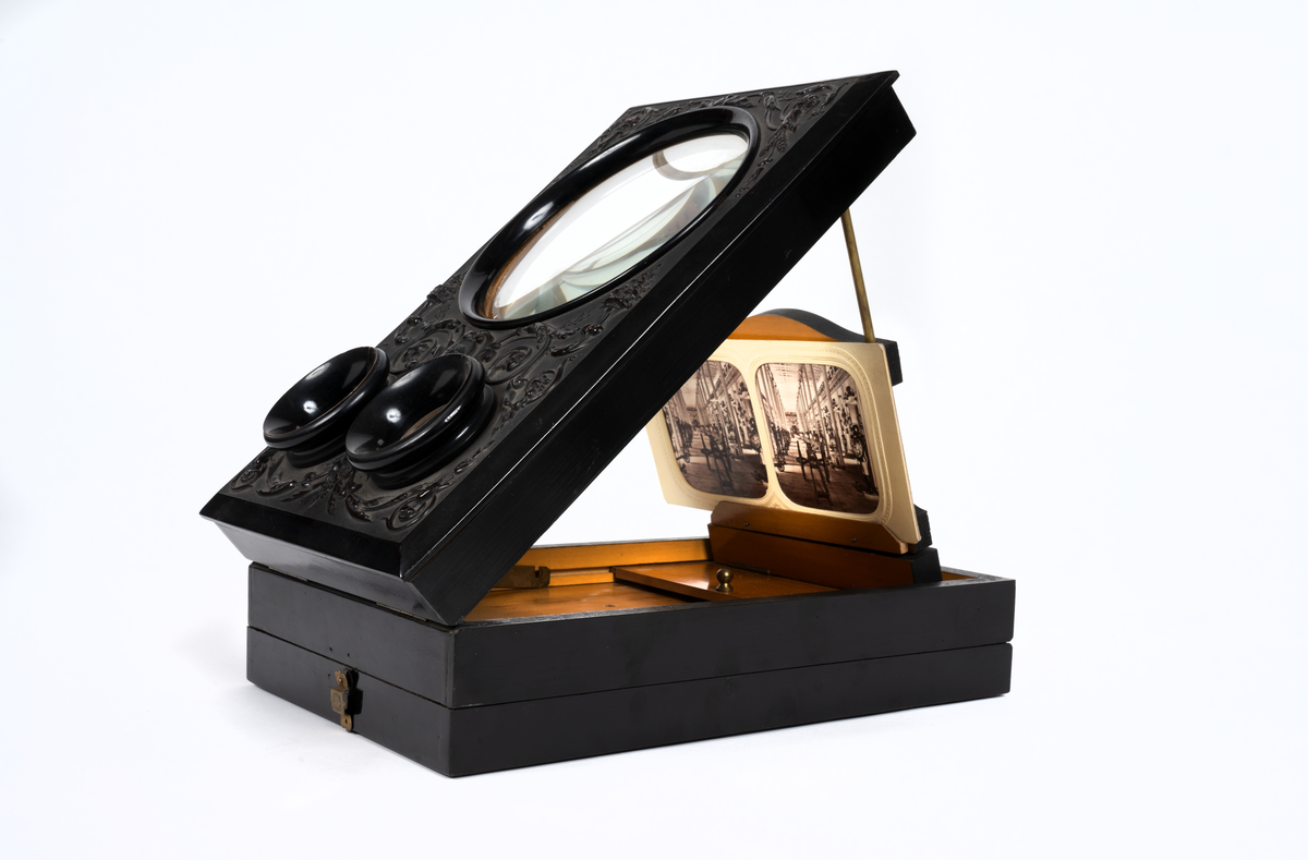 Svarlackad stereoskop med dekorerad ovansida och tre linser. Tillbehör finns.