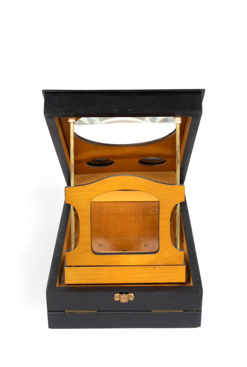 Svarlackad stereoskop med dekorerad ovansida och tre linser. Tillbehör finns.