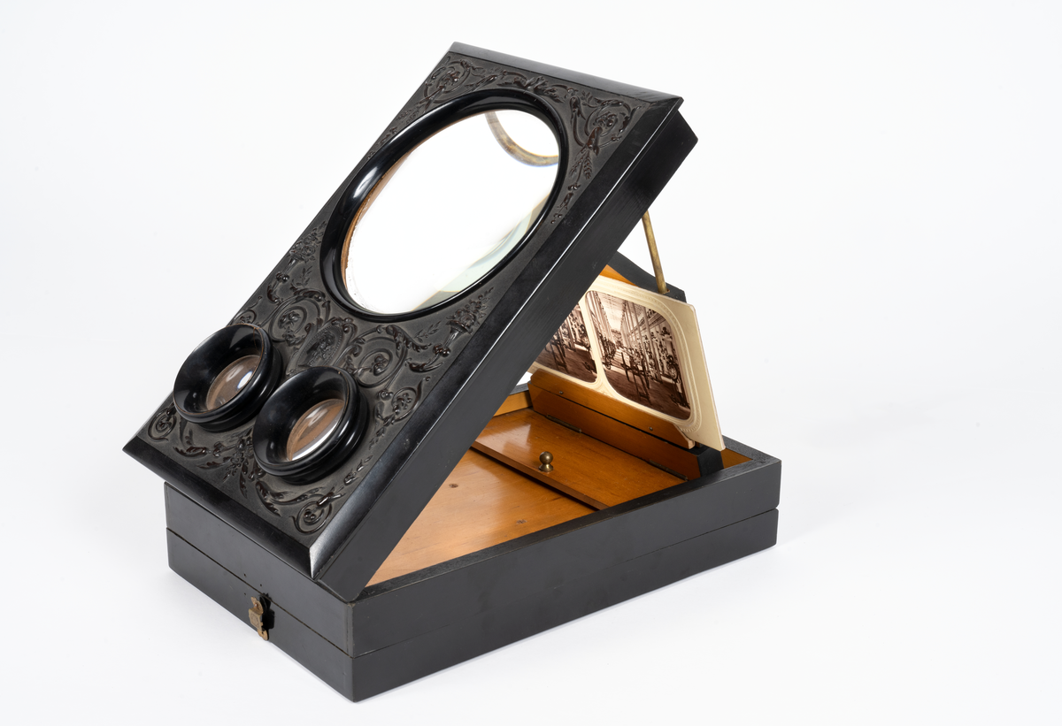 Svarlackad stereoskop med dekorerad ovansida och tre linser. Tillbehör finns.