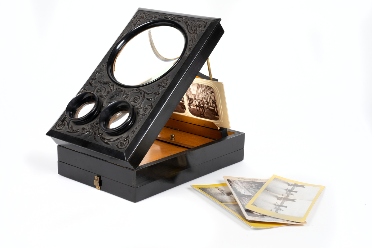 Svarlackad stereoskop med dekorerad ovansida och tre linser. Tillbehör finns.