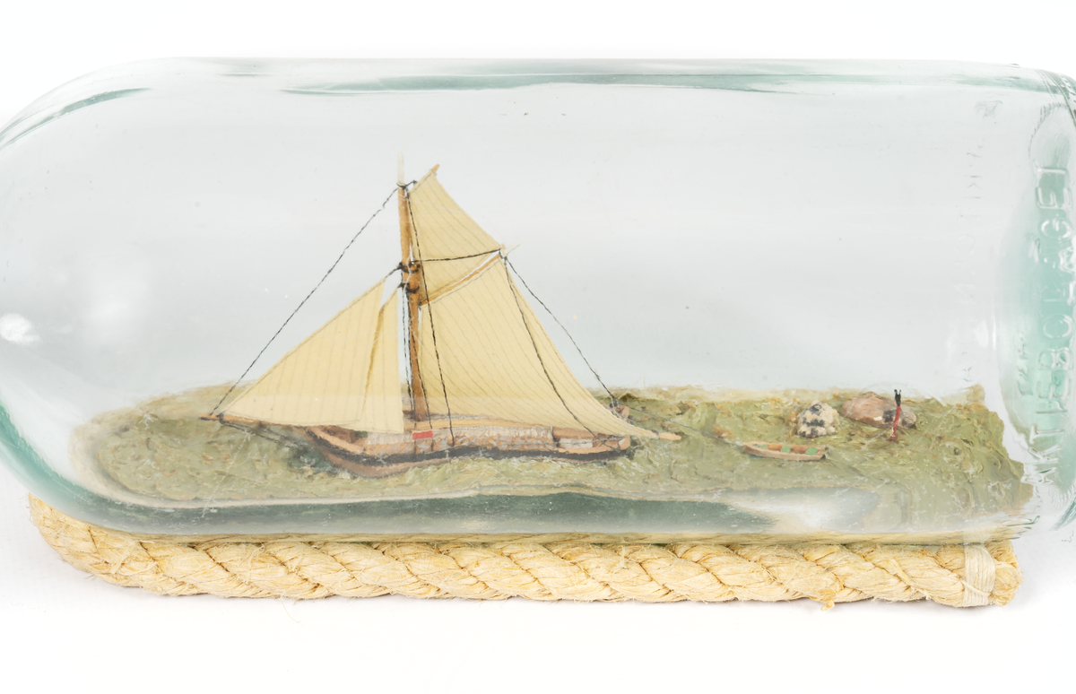 Flaskskepp av roslagsskuta under segel med gaffelstorsegel, gaffeltoppsegel, fock, klyvare. Jolle på släp. Skrå av otjärat rep.