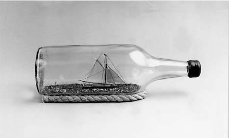 Flaskskepp av roslagsskuta under segel med gaffelstorsegel, gaffeltoppsegel, fock, klyvare. Jolle på släp. Skrå av otjärat rep.