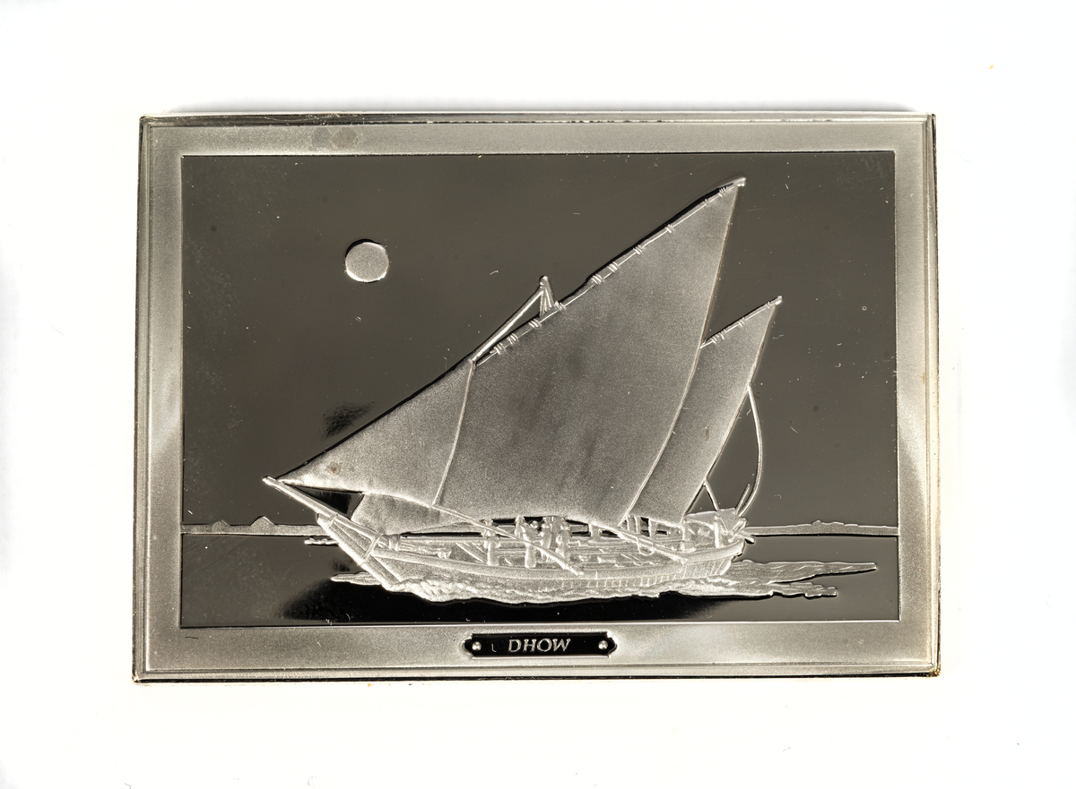 Rektangulär silverplakett föreställande en dhow från 1900-talet. Dhow är ett samlingsnamn för flera båttyper som används längs Indiska oceanens kuster på Arabiska halvön, längs Afrikas östkust, och kring Indiska halvön. Dhowerna kännetecknas av sina trekantiga latinsegel på framåtlutade master.
