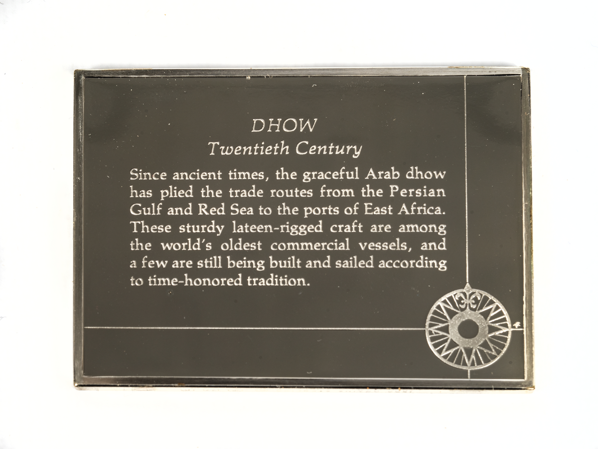 Rektangulär silverplakett föreställande en dhow från 1900-talet. Dhow är ett samlingsnamn för flera båttyper som används längs Indiska oceanens kuster på Arabiska halvön, längs Afrikas östkust, och kring Indiska halvön. Dhowerna kännetecknas av sina trekantiga latinsegel på framåtlutade master.