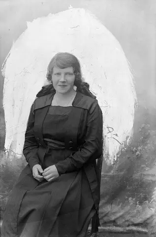 Portrett av en sittende kvinne. Hun har kjole på seg.