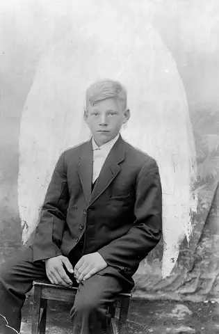 Portrettav en sittende gutt. Han har dress på seg.