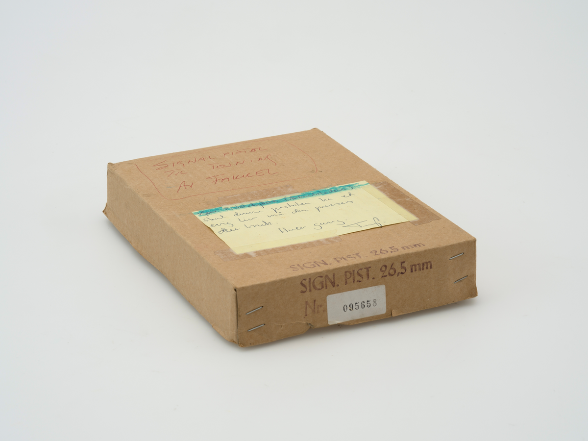 Eske med lokk til oppbevaring av signalpistol. Esken er en del av den originale emballasjen og har informasjon om pistolen stemplet på. Tekst og beskjeder om bruk er skrevet på for hånd flere steder på esken. Innvendig i esken ligger innpakningspapir som sannsynligvis er en del av den originale emballasjen.