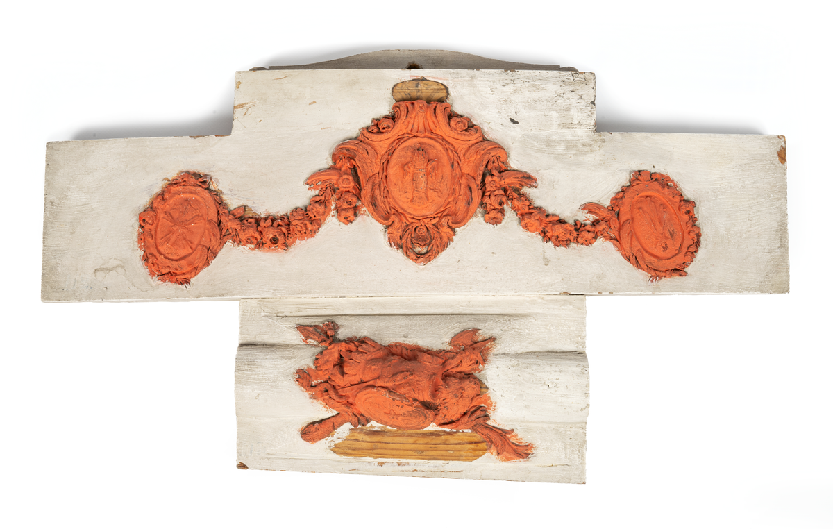 Akterspegelsornament, okänt fartyg. Vapensköld med stjärna och strålknippen, krönt bröstharnesk samt bila, svärd och lans, allt vilande på utbrett lejonhuvud. Monterad på kupig träplatta: 460 x 260 mm

Bildens övre ornament: O 02436
Bildens nedre ornament: O 02435