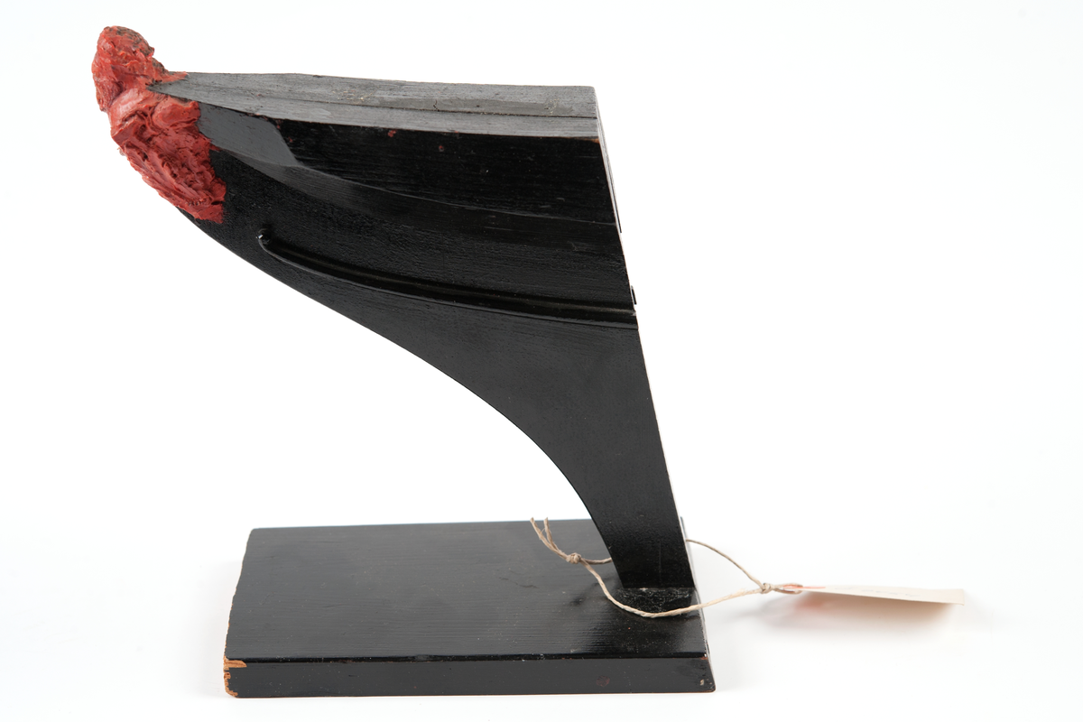 Ångkorvetten THORs galjon. Bröstbild av guden Thor  med hammare och brandfackla, samt akantusblad. Modelleringen skisserad. Monterad på stävkonstruktion av svartmålat trä, fästad till platta. Platta: 175x100 mm. Röd vax.