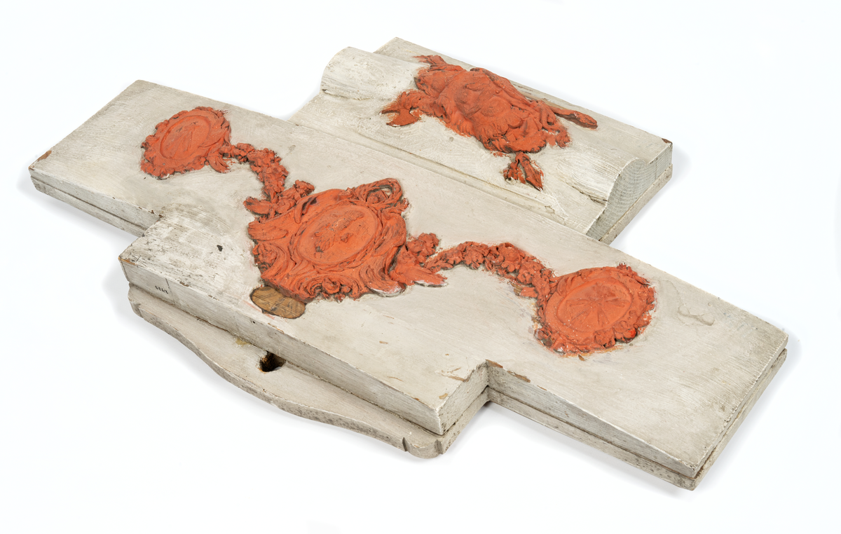 Akterspegelsornament, okänt fartyg. Vapensköld med stjärna och strålknippen, krönt bröstharnesk samt bila, svärd och lans, allt vilande på utbrett lejonhuvud. Monterad på kupig träplatta: 460 x 260 mm

Bildens övre ornament: O 02436
Bildens nedre ornament: O 02435