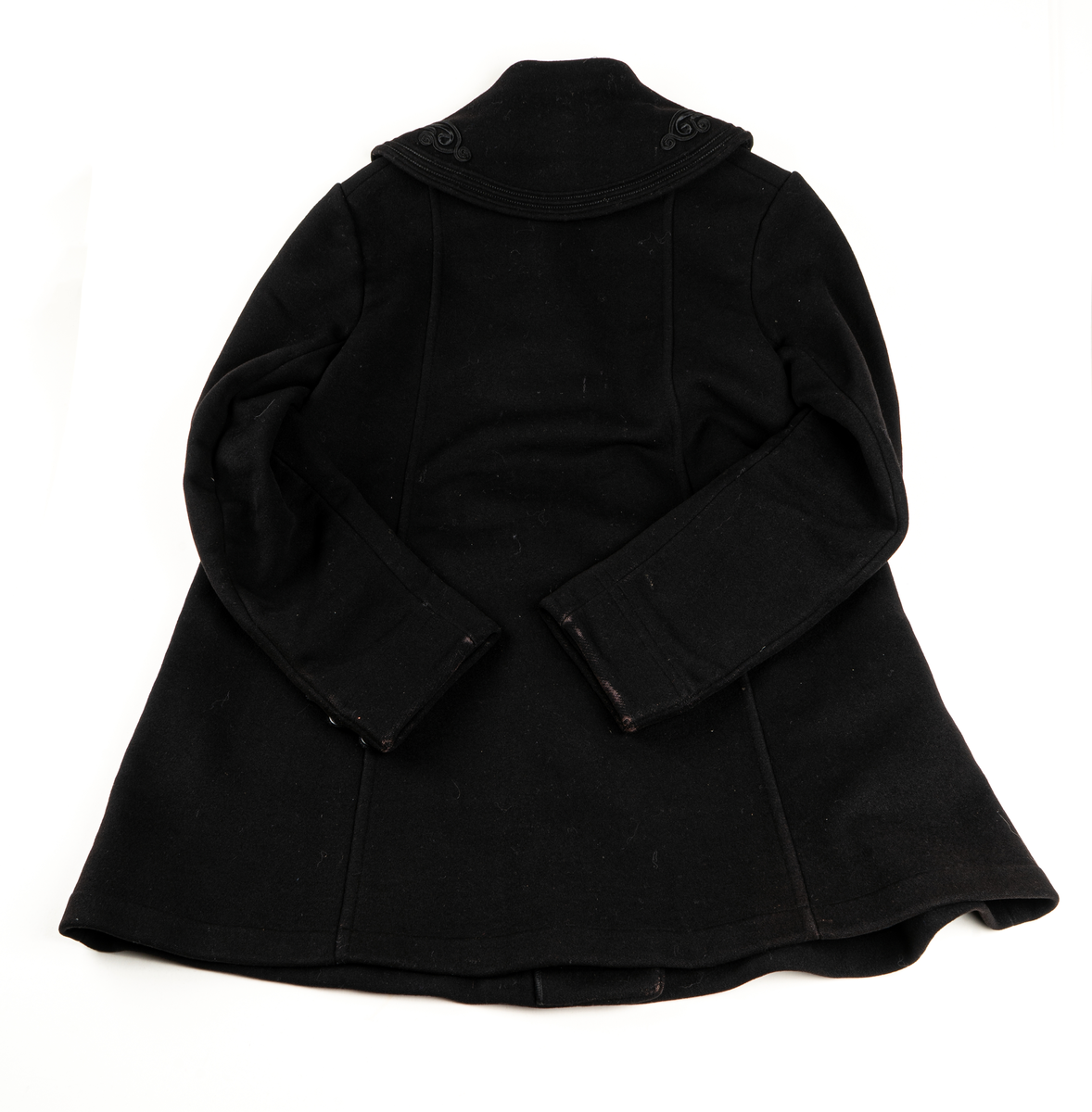 Svart kappa. Sjalkrage med snörbroderier och klädda knappar. Större oklädda knappar framtill.