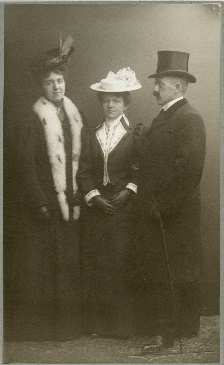 Porträtt av två kvinnor och en man i finkläder.