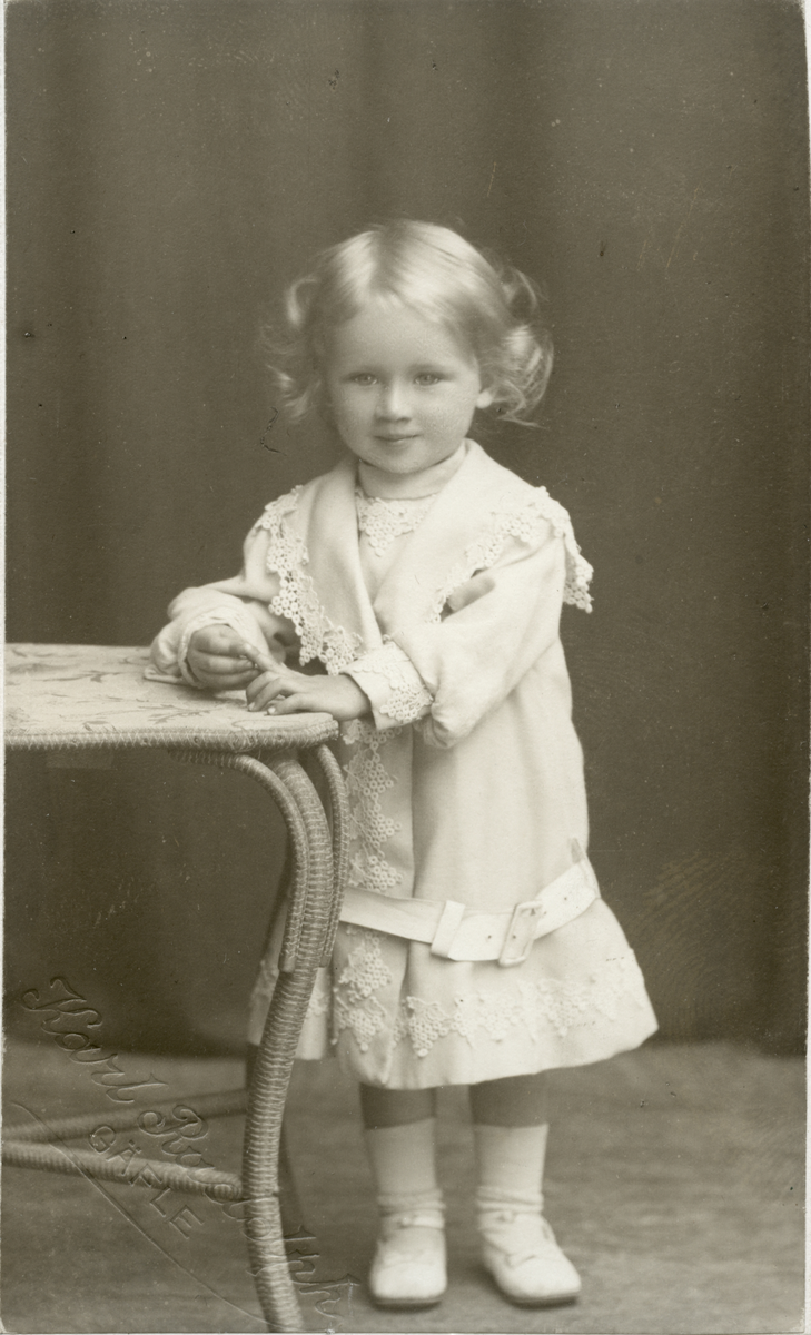 Porträtt av ett barn klädd i en kappa med spetsdetaljer.