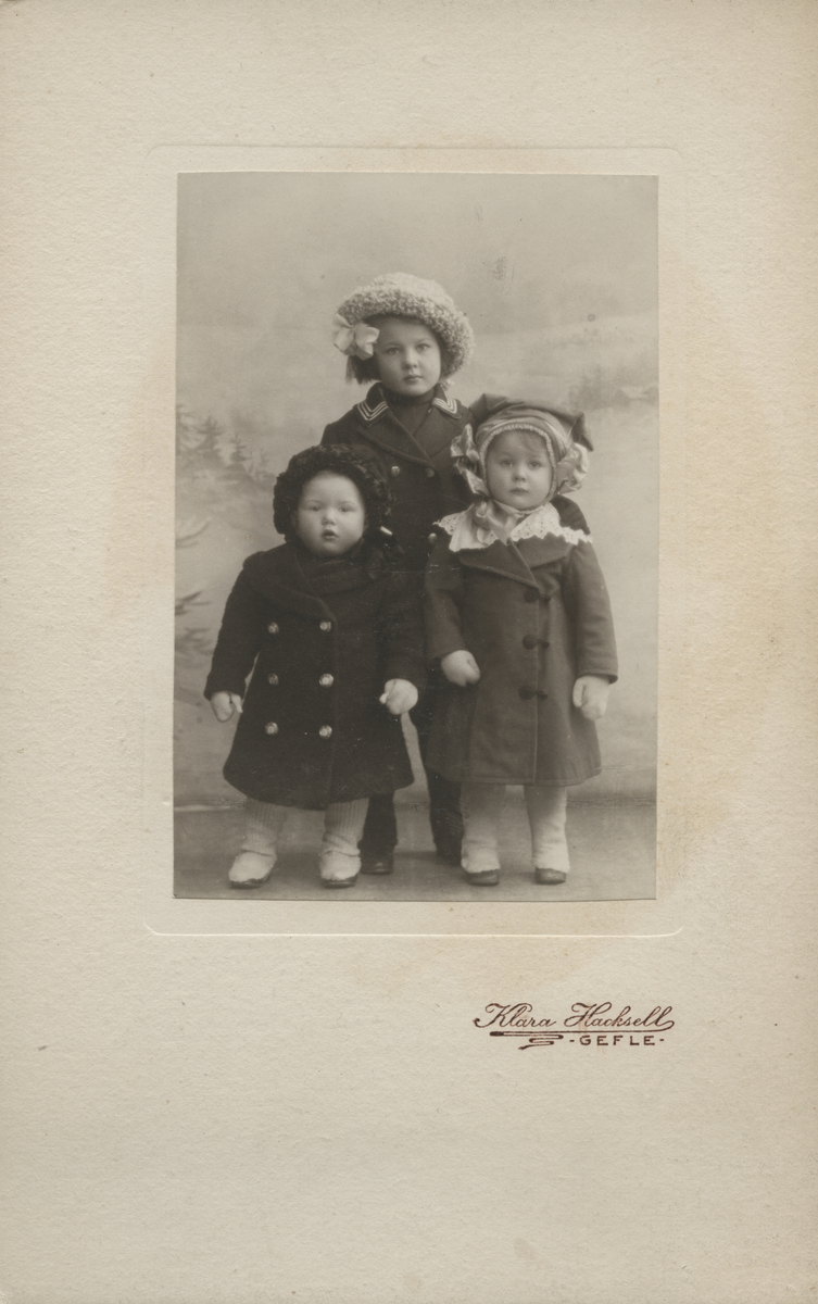 Porträtt av tre små barn klädda i vinterkläder.