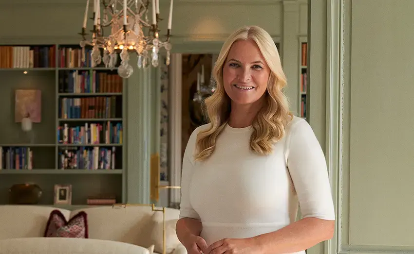 Bilete av kronprisesse Mette-Marit i ei stove med kvit kjole og bølga hår