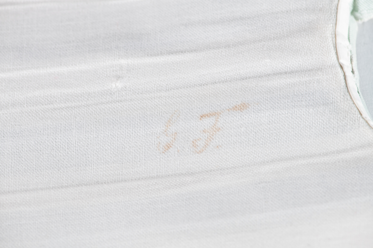 Løst skjortebryst i barnestørrelse.  Hvit med brede, grønne striper. Midtfold og to sidefolder. Påskrevet  G. F., som står for Gjeruld  Fløistad. Med vaskeblekk: 14. 