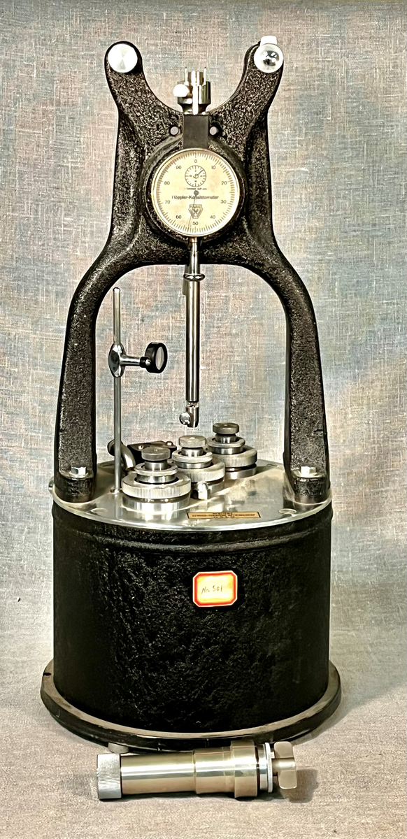 Apparat et består av et termostatbad med portalbrooverdel. På broen er en vertikal støt- eller trykkakse som presses ned av utskiftbare lodder montert på en vektarm. Aksens bevegelse overføres til et måleur, "1 teilstreich 0,01 mm". Badet har tre åpninger med innsatte prøvesylindere. Den midterste har sentral toppåpning i trykkaksens forlengelse.