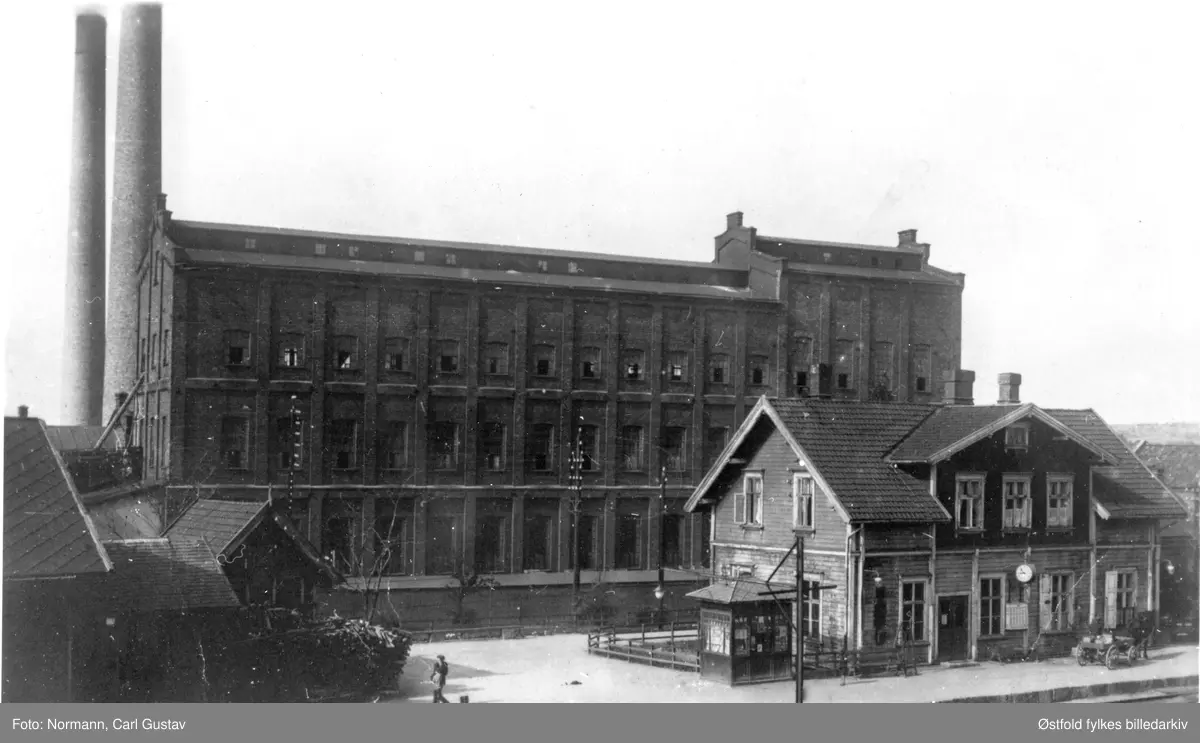 Greåker jernbanestasjon med kiosk. Bak AS Greaaker Cellulosefabrik,  Tune 1919.